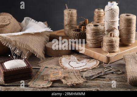 Pieces of burlap fabric, spools of twine and different sewing tools on wooden table Stock Photo
