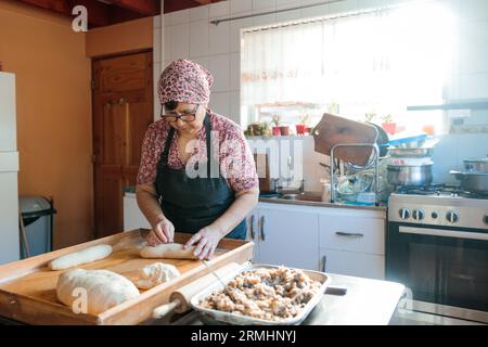Unrecognizable Latin Elderly Woman Kneading Dough with Hands and Rolling Pin in Her Countryside Kitchen Stock Photo