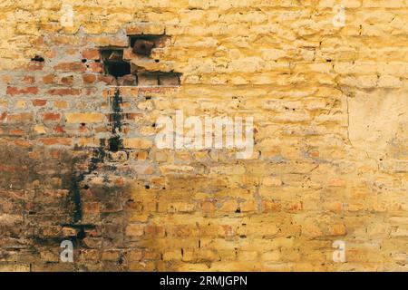Old cracked and dirty yellow brick wall background with unique worn texture and pattern of the surface as abstract backdrop for design Stock Photo