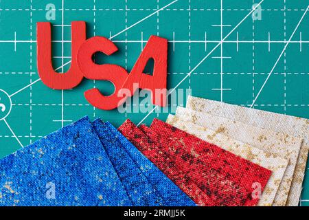 Wooden letters consisting to the abbreviation USA and square pieces of fabric in the US flag colors on a green craft mat Stock Photo