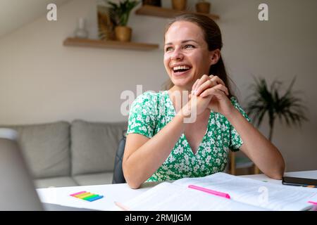 happy young adult elegant woman in green dress sitting at the table at home and laughing. Stock Photo
