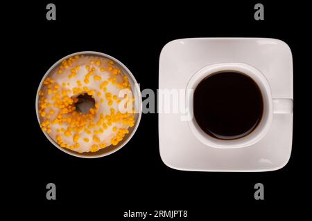 Doughnut with colorful sprinkles and cup of coffee isolated on pure dark black background. Treat of sweetness standing alone on solid backdrop. Stock Photo