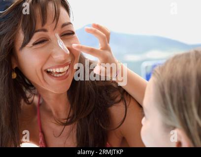 Daughter applying sunscreen lotion on mother nose Stock Photo