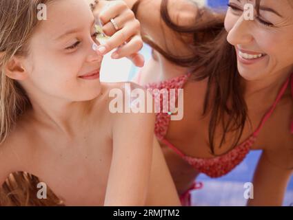 Mother applying sunscreen lotion on daughter nose Stock Photo