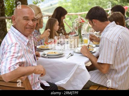 Extended family sitting at table having pasta meal with granddad in foreground Stock Photo