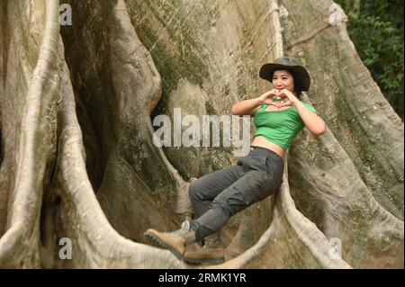 Beautiful Asian woman Posing in a standing and happy pose at the base of a big tree. And this tree is very large and is a popular attraction. Stock Photo