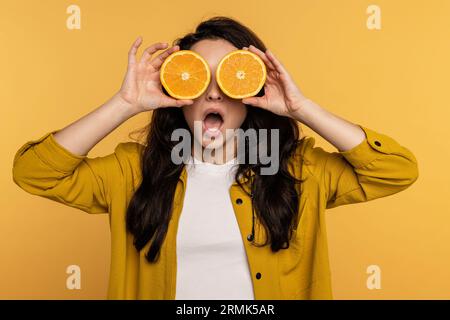 Mischievous dark-haired young woman hiding her face behind the juicy orange slices during the studio photo shoot. Healthy lifestyle concept Stock Photo