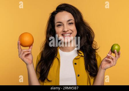 Joyous young woman posing for the camera with a couple of citrus fruits on the yellow background. Healthy eating concept Stock Photo