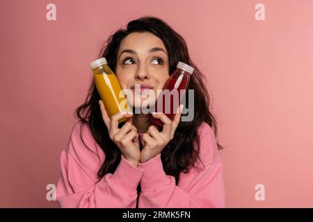 Dreamy young dark-haired woman posing for the camera on the pink background with bottled beverages in her hands. Healthy drink concept Stock Photo