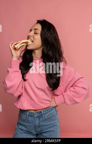 Hungry beautiful young dark-haired Caucasian woman snacking on an appetizing nutritious sandwich in front of the camera. Nourishing nutrition concept Stock Photo