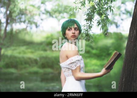 elegant green-haired girl reading a book in the quiet of a green park women in a green surreal atmosphere Stock Photo