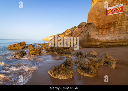 ROCKFALL UNSTABLE CLIFFS, KEEP A SAFE DISTANCE is written in English on a warning sign in Portugal on the cliffs of the Atlantic Ocean. Rocks and Stock Photo
