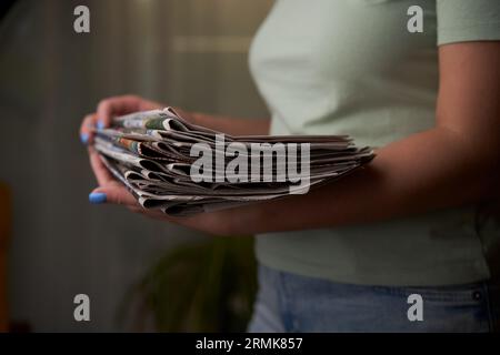 A woman stacks old newspapers in a pile, waste paper collect. Preparing paper waste for recycling. Stock Photo