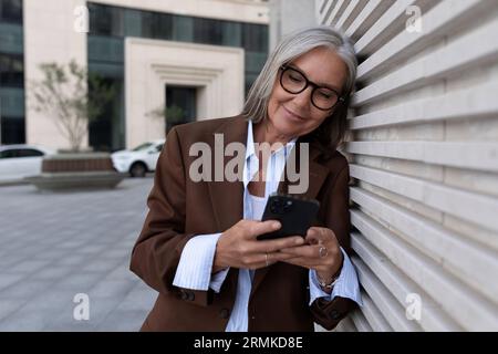 charming successful senior woman with gray hair and glasses is dressed in a brown designer suit Stock Photo