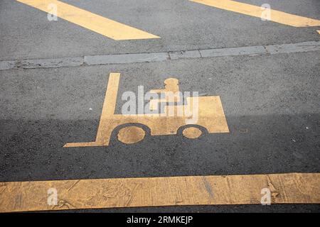 A yellow forklift safety symbol on black asphalt road indicating transportation loading Stock Photo