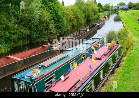 Line of historic narrowboats being pulled past two moored narrowboats is seen from above. Stock Photo