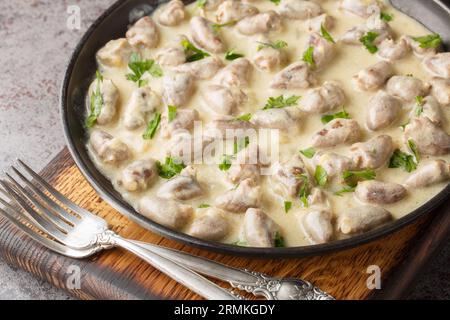 Tender stewed chicken hearts in garlic cream sauce with herbs close-up in a plate on the table. Horizontal Stock Photo