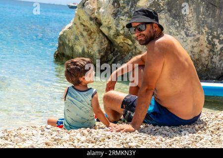 Portrait of father and son playing on the beach of Paralia Mikros Gialos in Lefkada, throwing stones. Greece Stock Photo