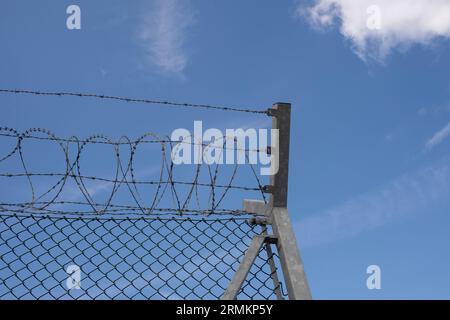 Metal fence with barbed wire against a blue sky background Stock Photo