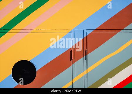 A colorfully painted, vintage appearing, wall of angles stripped pattern with doors and a port window, horizontal Stock Photo