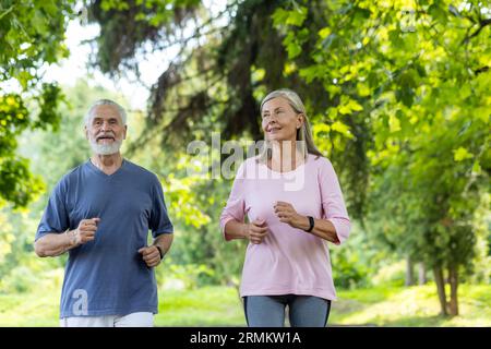 Senior couple of pensioners jogging in the park, gray-haired man and woman joyfully running, active lifestyle. Stock Photo