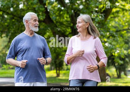 Senior couple of pensioners jogging in the park, gray-haired man and woman joyfully running, active lifestyle. Stock Photo