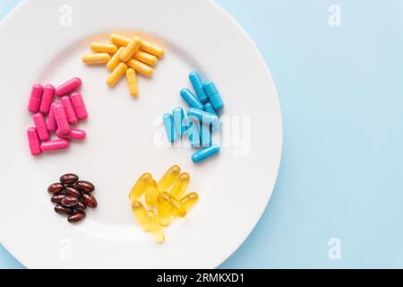 Food supplements of bright color lie on a white plate on a blue background. Concept of health support and lack of vitamins Stock Photo