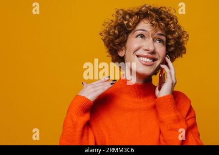 Cheerful middle-aged woman talking on cellphone isolated over yellow wall Stock Photo