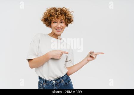Cheerful ginger middle-aged woman pointing fingers at copyspace isolated over white studio background Stock Photo