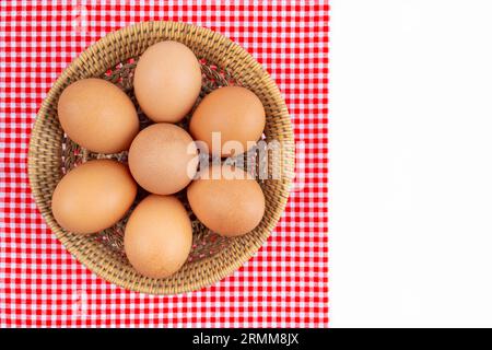 Fresh farm eggs in wooden weave basket with red tablecloth isolated on white background, and copy space for your text. Stock Photo
