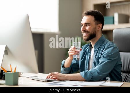 Handsome young businessman drinking water and working on computer in office Stock Photo