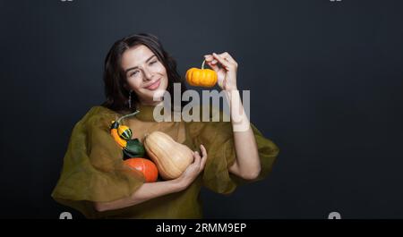 Pretty young woman holding a pumpkin against black studio wall background Stock Photo