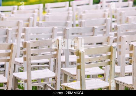 Elegant Garden Celebration: White chairs arranged on the lush green grass create a charming wedding ceremony setting amidst nature's backdrop. Stock Photo