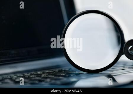 Laptop computer with keyboard and magnifying glass on top, representing the process of search at the internet, combining old and new concepts Stock Photo