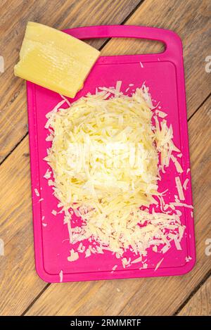 Top view of a pile of grated cheese on a plastic cutting board. Wooden background, copy space. Stock Photo