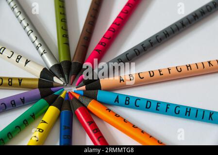 Different colored crayons with letters arranged in a circle on white background. Colourful nice graphic concept. Stock Photo