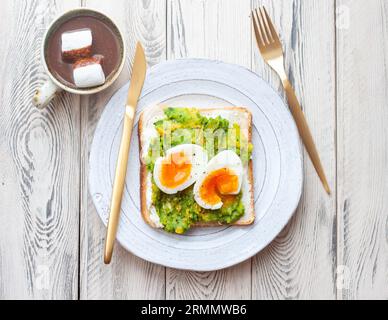 Avocado egg sandwich with a cup of hot cocoa. Healthy light breakfast concept. Whole grain toasts with mashed avocado and fried eggs and pumpkin seeds Stock Photo