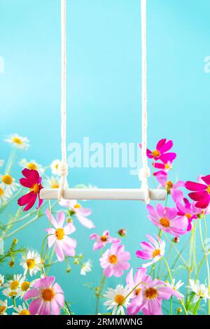 Swing with flowers on a blue background. Summer scene mockup for the presentation of goods and cosmetics. Stock Photo