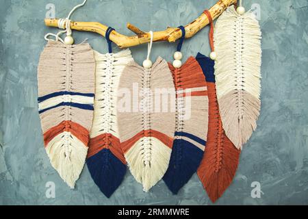 Wall panel in Boho style made of cotton beige, blue and red cords using macrame technique. Modern home decor trend, cozy atmosphere, gray background. Stock Photo