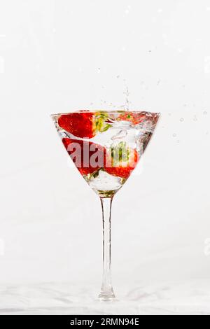 A glass of alcoholic beverage with ripe strawberries floating in it, splashes of liquid cascading down the sides Stock Photo