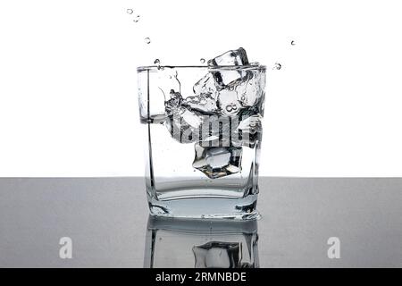 Cold water in a glass with ice cubes. Water splash. Relax on a hot summer day. Monochrome image. Stock Photo
