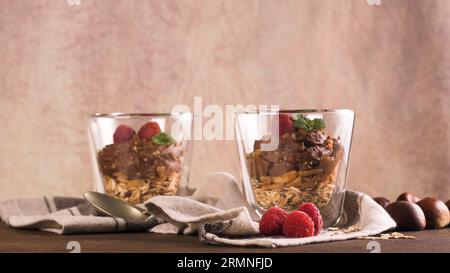 Couple of glasses of chocolate and chestnuts mousse with roasted almonds and oats decorated with raspberries and mint leaves. Stock Photo