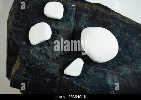 four white smooth stones laying over one black flat stone surface Stock Photo