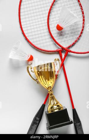 Gold cup with badminton rackets and shuttlecocks on light background Stock Photo