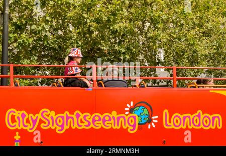 London, England, UK - 24 August 2023: Visitors to London sitting on the top deck of an open topped sightseeing bus wearing sun hats with a Union Jack Stock Photo