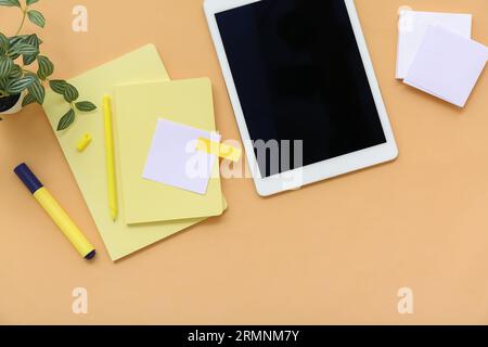 Tablet with notebooks and sticky notes on orange background Stock Photo