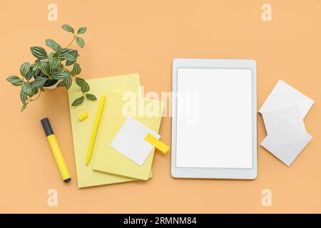 Tablet with notebooks and sticky notes on orange background Stock Photo