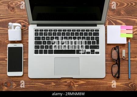 Laptop with eyeglasses, gadgets and stationery on brown wooden background Stock Photo
