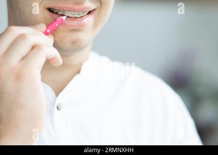 Handsome young man with beautiful white teeth with brackets cleaning his teeth with dental brush stick close up copy space. handsome young man with de Stock Photo
