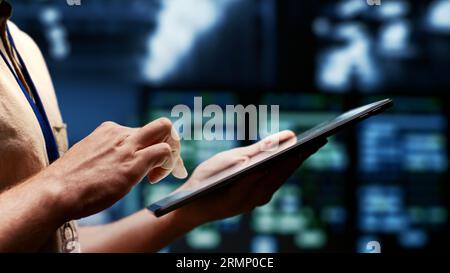 IT admin evaluating energy efficient server clusters using renewable sources to reduce electronics carbon footprint. Engineer typing on tablet in sustainable high tech facility, close up Stock Photo
